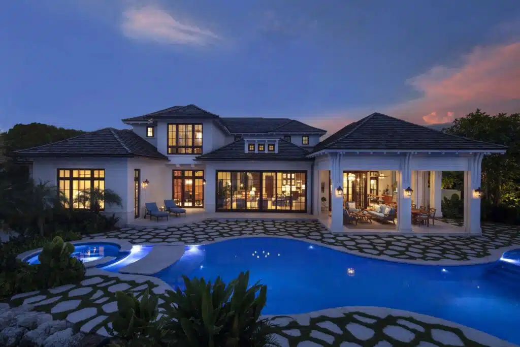 The lit pool and covered outdoor rooms of a member-built coastal home at dusk